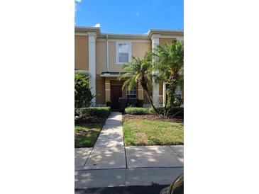 Tan two-story townhome with dark brown door, landscaping, and walkway at 652 Chelsea Dr, Davenport, FL 33897