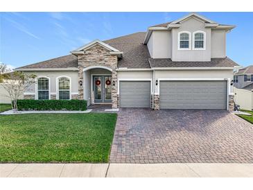 Two-story house with stone accents, three-car garage, and manicured lawn at 405 Amola Way, Howey In The Hills, FL 34737