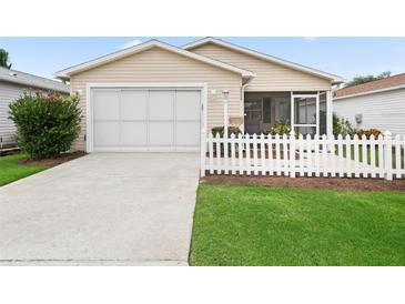 Tan house with white picket fence, attached garage, and landscaped lawn at 2404 Travis Pl, The Villages, FL 32162