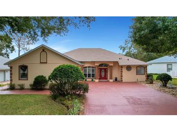 Single-story home with a red door, large driveway, and landscaped yard at 5509 Grove Mnr, Lady Lake, FL 32159