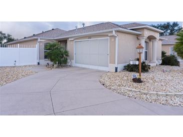 Tan house with white garage door, landscaping, and a long driveway at 1808 Dalton Dr, The Villages, FL 32162