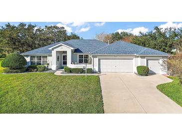 Single-story house with blue roof, two-car garage, and well-manicured lawn at 27437 Desert Rose Ct, Leesburg, FL 34748