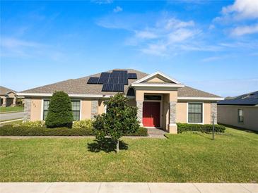 One-story home with solar panels, red front door, and landscaped yard at 303 Lake Mariana Pl, Auburndale, FL 33823