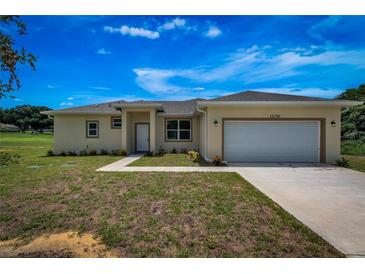 Front view of a single-story house with a beige exterior, two-car garage, and landscaped lawn at 15190 Cr-565A, Clermont, FL 34711