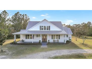 Charming farmhouse exterior with a metal roof, front porch, and landscaping at 153 Ashby Cove Ln, New Smyrna Beach, FL 32168