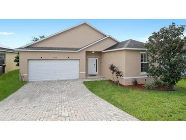 Tan house with a white garage door and brick paved driveway at 165 Captain Hook Way, Davenport, FL 33837