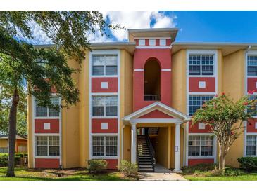 Two-story apartment building with terracotta and yellow exterior, landscaping, and stairs at 3502 Windy Walk Way # 2104, Orlando, FL 32837
