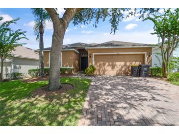 Tan one-story house with a two-car garage and well-manicured lawn at 619 Kensington Dr, Davenport, FL 33897