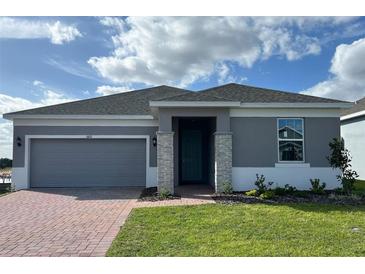One-story home with gray exterior, brick paver driveway and landscaping at 6821 Serpent Hawk Lane St, Howey In The Hills, FL 34737