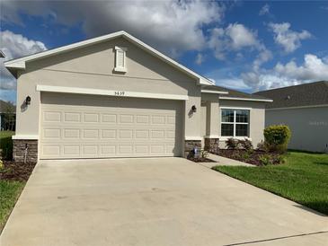 Beige house with a two-car garage and landscaping at 5639 Costa Blanca Way, Davenport, FL 33897