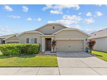 Tan house exterior with two-car garage and landscaping at 5716 Lakeside Landings Blvd, Winter Haven, FL 33881
