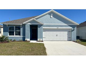 Newly constructed home featuring a light blue exterior, white garage door, and well-manicured lawn at 11567 Amber Ridge Dr, Zellwood, FL 32798