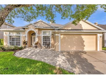 Tan one-story house with a paved walkway, two-car garage, and lush landscaping at 10946 Piping Rock Cir, Orlando, FL 32817