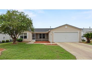 Tan one-story house with two-car garage, screened porch, and landscaping at 17394 Se 74Th Seabrook Ct, The Villages, FL 32162