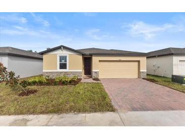 Tan house with dark brown roof, brick driveway and landscaping at 3206 Viceroy Ct, Poinciana, FL 34759