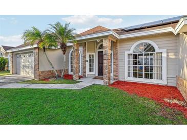 Tan brick house with dark brown door, solar panels, and manicured lawn at 1546 Thornhill Cir, Oviedo, FL 32765