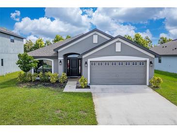 Gray house with a two-car garage and landscaping at 220 Bergamot Loop, Davenport, FL 33837