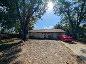 Ranch style home with a red car parked in the driveway, surrounded by large trees at 1301 Redwood Ct, Tavares, FL 32778