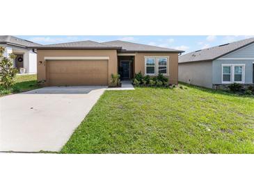 Tan one-story house with a two-car garage and green lawn at 928 Orchid Grove Blvd, Davenport, FL 33837