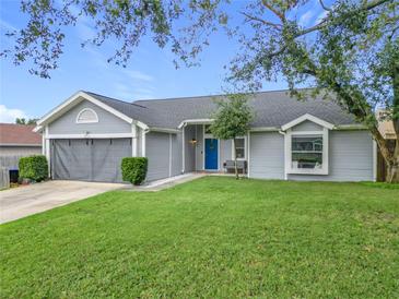 Gray house with a blue door, two-car garage, and well-manicured lawn at 7471 Crooked Lake Cir, Orlando, FL 32818