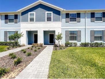 Two-story townhome with light blue and gray siding, a paved walkway, and a well-manicured lawn at 617 Jasmine Ln, Davenport, FL 33897