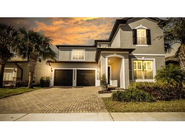 Two-story house with gray siding, dark garage doors, and a brick driveway at 7224 Enchanted Lake Dr, Winter Garden, FL 34787