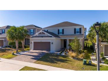 Two-story home with a brown garage door, palm trees, and landscaping at 2695 Plume Rd, Clermont, FL 34711