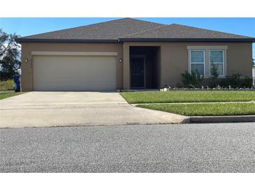 Tan one-story house with a two-car garage and a neatly landscaped lawn at 16344 Blooming Cherry Dr, Groveland, FL 34736