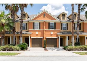 Front view of two story townhouses with attached garages, lush landscaping, and palm trees at 875 Assembly Ct, Reunion, FL 34747
