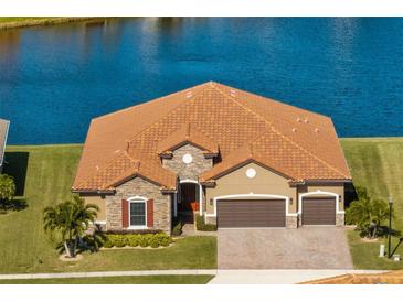 Single-story house with a brown tile roof, stone accents, and a two-car garage, situated by a lake at 4363 Summer Breeze Way, Kissimmee, FL 34744