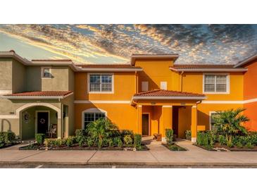 Two-story townhome with orange and green exterior, landscaping, and a walkway at 8931 Bismarck Palm Rd, Kissimmee, FL 34747