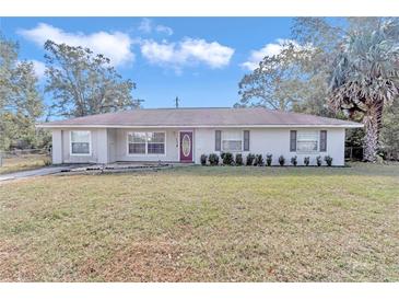 Ranch style home with red front door, well-manicured lawn and mature trees at 5724 Se 2Nd St, Ocala, FL 34480