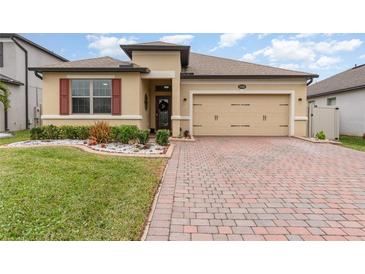 Tan one-story house with red shutters, two-car garage, and landscaped yard at 1380 Clear Brook Pl, St Cloud, FL 34772