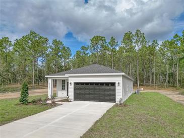 White house with black garage door and landscaping; in a wooded setting at 406 Nw Narcissus Rd, Dunnellon, FL 34431