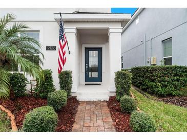 Front entry with brick walkway, American flag, and lush landscaping at 12128 Illustration Dr, Orlando, FL 32832