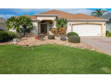 One-story home with landscaped yard, paver driveway, and two-car garage at 1757 Millwood Way, The Villages, FL 32162