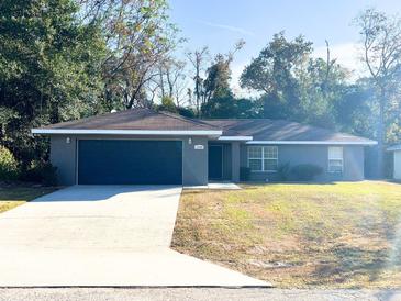 Gray house with a dark gray garage door and a well-maintained lawn at 13709 Se 40Th Ct, Summerfield, FL 34491