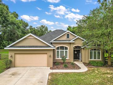 House exterior with a tan exterior, a two-car garage, and landscaping at 9680 Ne 25Th Ct, Anthony, FL 32617
