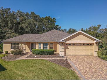 Single-story house with a tan exterior, brick driveway and landscaped yard at 13166 Se 86Th Cir, Summerfield, FL 34491