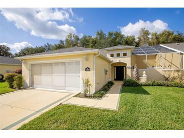 House exterior featuring a yellow facade, a three-car garage, and a well-manicured lawn at 15659 Sw 13Th Cir, Ocala, FL 34473