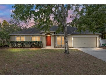 Tan one-story house with red door, attached garage, and landscaping at 20390 Sw 57Th St, Dunnellon, FL 34431