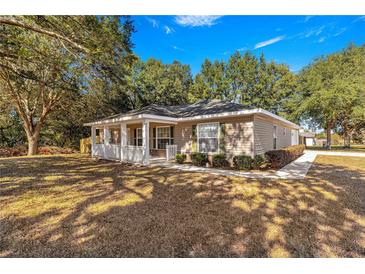 Tan house with white porch and landscaping, a long driveway and mature trees at 6845 Se 52Nd St, Ocala, FL 34472