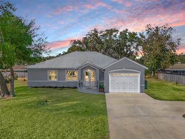 Gray house with metal roof, white garage door, and landscaped lawn at 1166 Cr 441, Lake Panasoffkee, FL 33538