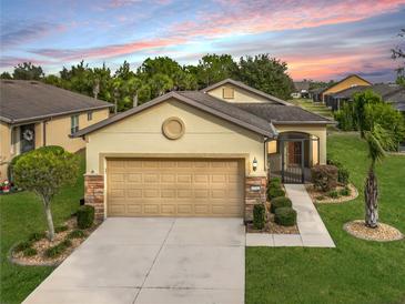 Tan house with a two-car garage and landscaped lawn at 7732 Sw 94Th Cir, Ocala, FL 34481