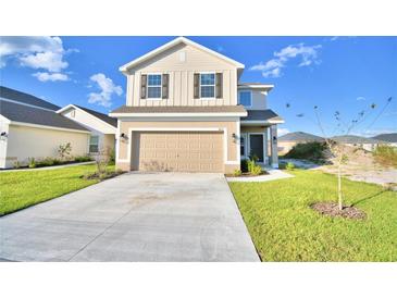 Two story house with tan siding, a two car garage, and landscaping at 1472 Leamington Ln, Winter Haven, FL 33884