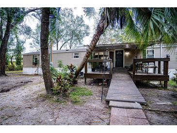 Tan mobile home with covered deck, ramp, and mature landscaping at 2419 Trenton E Rd, Lakeland, FL 33815