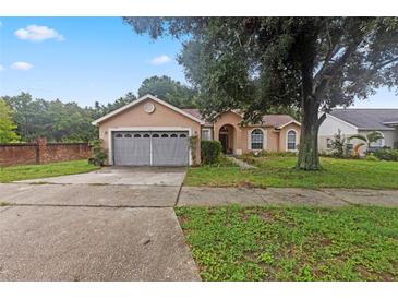 Tan two-car garage home with mature tree in the front yard at 2771 Cedaridge Cir, Clermont, FL 34711