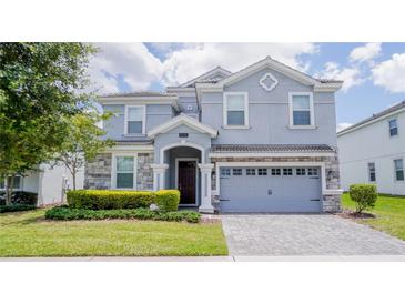 Two-story house with gray siding, stone accents, and a three-car garage at 1676 Moon Valley Dr, Davenport, FL 33896