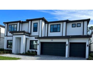 Two-story house with a modern design, featuring a white facade, dark gray garage doors, and black window frames at 1427 Butterfly Milkweed, Davenport, FL 33837