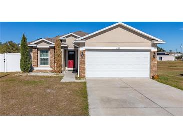 Tan house with red door, white garage door, and landscaping at 825 Desmoines Pl, Kissimmee, FL 34759